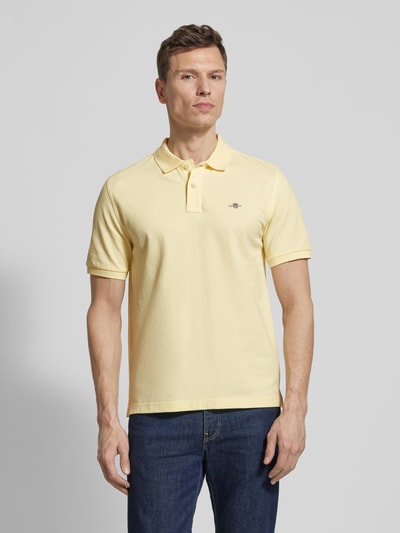 Männermodel trägt Slim Fit Poloshirt mit Logo-Stitching von Gant in Gelb, reine Baumwolle, kurzärmelig, Ganzkörperansicht von vorne.