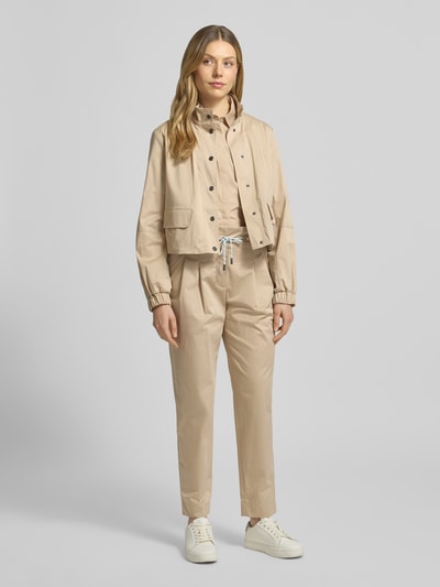 Kobiece modelka nosi Boxy Fit Bluse mit Brusttaschen von Marc Cain z bawełny, kołnierzyk koszulowy, listwa guzikowa, brustasza, długość tyłu 51 cm, długość rękawów 57 cm, jasny beż, faktura gładka, prostokątne kształty, Ganzkörperansicht von vorne.