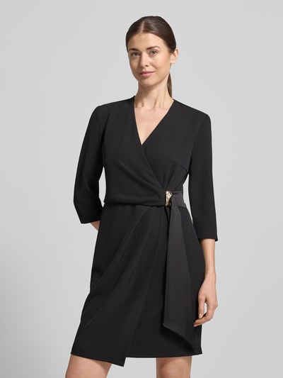 Modelka kobieca ma na sobie Knielanges Cocktailkleid in Wickel-Optik von Rinascimento, czarna mieszanka materiałów z dodatkiem streczu, prosty krój, długość do kolan, kopertowy styl, rękaw o dł. 3/4, długość tyłu w rozmiarze S: 90 cm, szerokość w rozmiarze S: 46 cm, długość rękawów w rozmiarze S: 44 cm, gładka tekstura, bez wzorów, całkowity widok z przodu