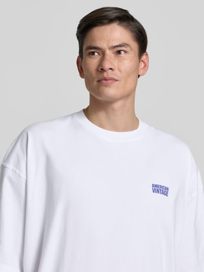 Männermodel trägt weißes Herren T-Shirt mit Logo-Print von American Vintage, Reine Baumwolle, Loose-Fit, Nahaufnahme Oberkörper. Modell 'GIXY', Rundhalsausschnitt, Rückenlänge 72 cm bei Größe M/L.
