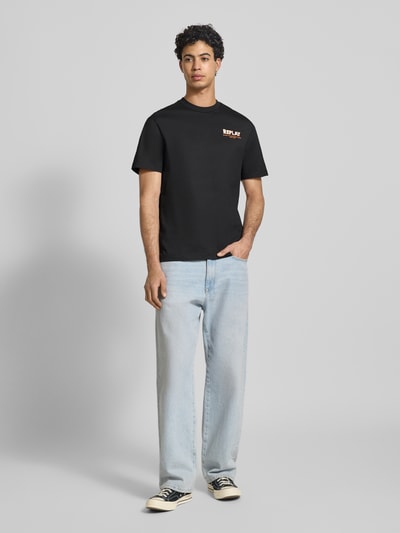 Męski model nosi Regular Fit T-Shirt mit Logo-Stitching od Replay z bawełny, nadruk z napisem, okrągły dekolt, długość tyłu 70 cm, ganzkörperansicht von vorne.