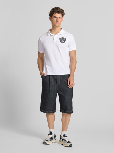 Männermodel trägt Regular Fit Poloshirt mit Label-Patches von Superdry in Weiß, Reine Baumwolle, Polokragen, kurze Knopfleiste, Ganzkörperansicht von vorne. Rückenlänge bei Größe M: 68 cm.