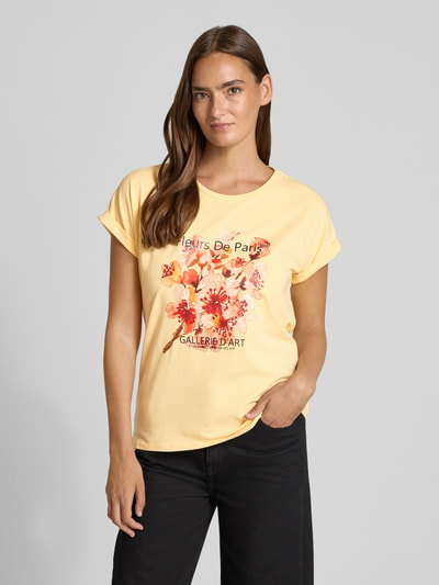 Frauenmodel trägt Damen T-Shirt mit Motiv-Print Modell 'RINA' von Soyaconcept in Gelb, aus Baumwoll-Elasthan-Mix, Regular-Fit, Rundhalsausschnitt, Ärmel mit Aufschlag, Rückenlänge 61 cm bei Größe S, Motiv-Print in Rot- und Orangetönen, glatte Textur. Ganzkörperansicht von vorne.