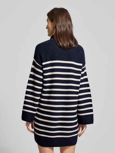 Frauenmodel trägt Mini-Strickkleid aus Woll-Kaschmir-Mix Modell 'AREENA' von Lauren Ralph Lauren, navy mit weißen Streifen, oversized, gerippte Abschlüsse, Rollkragen, Minilänge, Rückenlänge 83 cm, Ärmellänge 67 cm, Ganzkörperansicht Rückansicht.