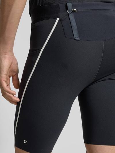 Männermodel trägt Tights mit Logo und Reißverschlusstasche von Salomon, Schwarz mit weißen Akzenten, Material-Mix, Detailaufnahme Rückansicht.