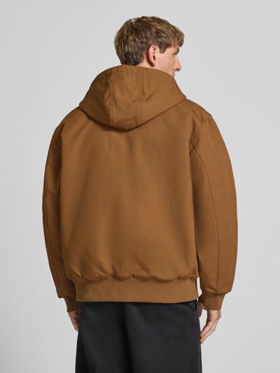 Männermodel trägt Jacke mit Label-Patch und Känguru-Tasche von Carhartt Work In Progress in Braun mit Kapuze, Rückansicht, Ganzkörperansicht Rückansicht. Reine Baumwolle, Regular Fit, gerippte Abschlüsse, sichtbare Textur.