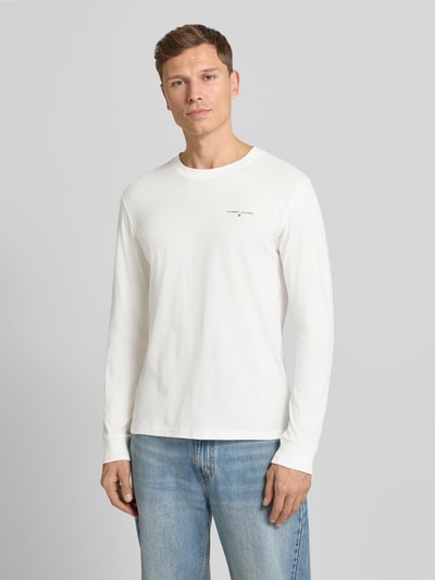 Männermodel trägt Slim Fit Langarmshirt aus reine Baumwolle von Tommy Jeans, Optik: Unifarben, Label-Schriftzug, Ganzkörperansicht von vorne.