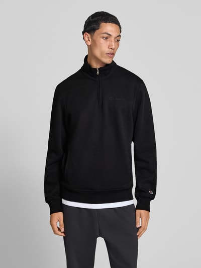 Männermodel trägt Sweatshirt mit Label-Details von Champion in Schwarz, Troyer-Kragen, Baumwollmischung, Ganzkörperansicht von vorne.