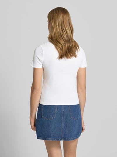 Frauenmodel trägt T-Shirt mit Motiv-Print Modell 'GIGI' von JJXX aus weißem Baumwoll-Mix, gerade Passform, Rock, Ganzkörperansicht Rückansicht.