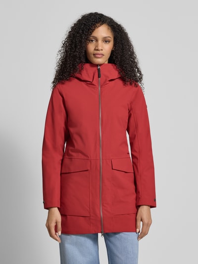 Frauenmodel trägt roten Regular Fit Parka mit Logo-Applikation Modell 'Folka' von Didriksons, aufgesetzte Taschen, Zweiwege-Reißverschluss, Ganzkörperansicht von vorne.