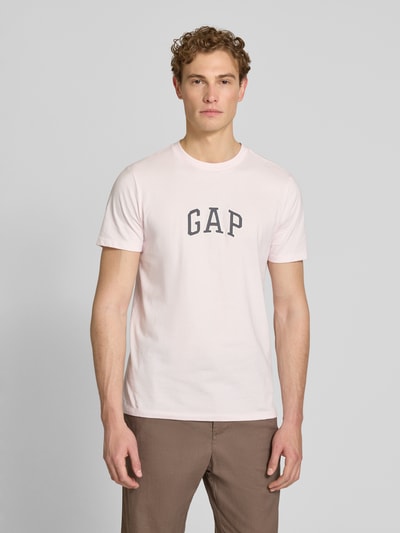 Männermodel trägt T-Shirt mit Logo-Patch und Rundhalsausschnitt von GAP in Hellrosa, reine Baumwolle, Straight Fit, Ganzkörperansicht von vorne.