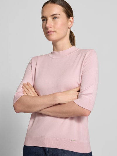 Frauenmodel trägt Strickpullover aus Viskose-Mix von MORE & MORE in Rosa, taillierte Passform und Stehkragen, Nahaufnahme Oberkörper.