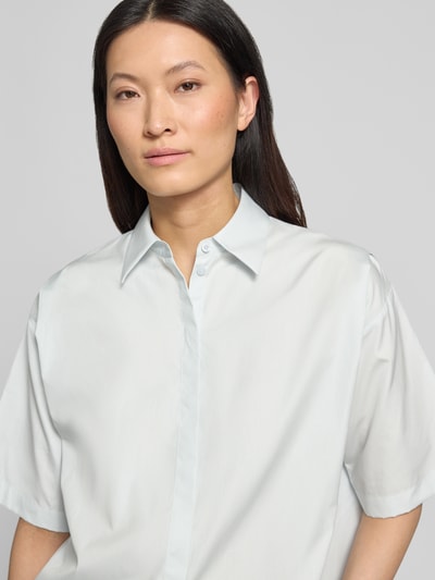 Frauenmodel trägt Oversized Hemdbluse aus reiner Baumwolle Modell 'BIMINA' von BOSS in Optik: Unifarben mit Hemdkragen und Label-Detail, gefertigt aus Popeline mit verdeckter Knopfleiste und Kurzarm, Nahaufnahme Oberkörper.