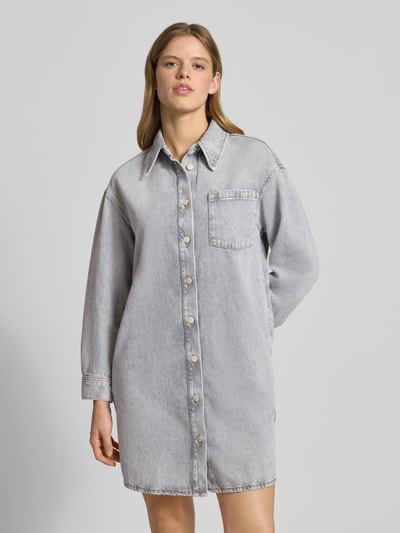 Frauenmodel trägt Loose Fit Jeanskleid aus reiner Baumwolle von Marc O'Polo Denim in grauer Denim-Optik mit Brusttasche, Mini-Länge, Langarm, Manschette, Rückenpasse, Ganzkörperansicht von vorne.