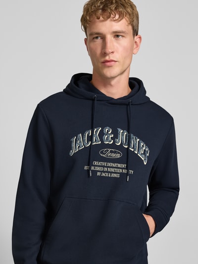 Männermodel trägt Regular Fit Hoodie aus Baumwoll-Mix Modell 'Denver' von JACK & JONES in Dunkelblau mit Känguru-Tasche, Nahaufnahme Oberkörper.