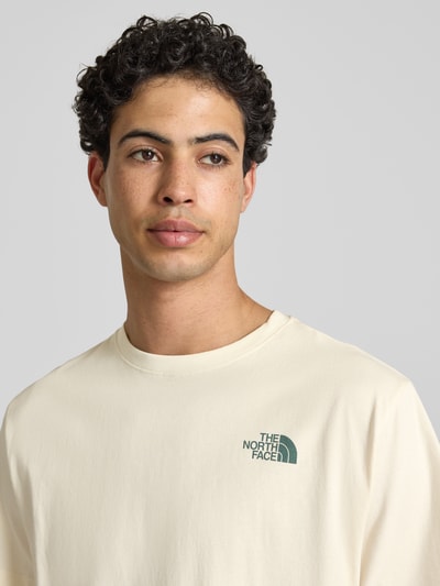 Męski model nosi Relaxed Fit T-Shirt mit Logo-Print von The North Face, bawełna, okrągły dekolt, kremowy, nadruk z logo, długość tyłu 70 cm w rozmiarze M, zbliżenie na górną część ciała