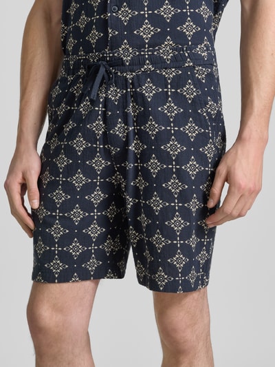 Mannenmodel draagt Relaxed Fit Stoffshorts uit katoen van s.Oliver RED LABEL in donkerblauw met beige patroon, detailopname heupen.