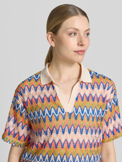 Frauenmodel trägt Boxy Fit T-Shirt mit Polokragen und V-Ausschnitt von Smith and Soul, Allover-Look mit Strukturmuster, bunte Zickzack-Muster, Nahaufnahme Oberkörper.