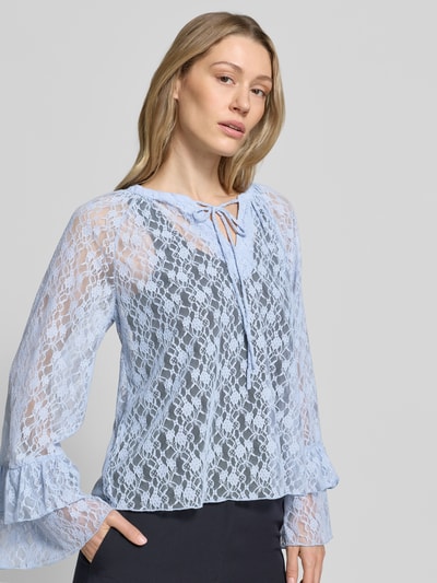Frauenmodel trägt Regular Fit Langarmbluse in Spitzen-Optik Modell 'LOULOU' von Vero Moda in Semitransparente-Optik mit Trompetenärmeln, V-Ausschnitt, Schleifenverschluss, Materialverarbeitung Spitze, Ganzkörperansicht von vorne.