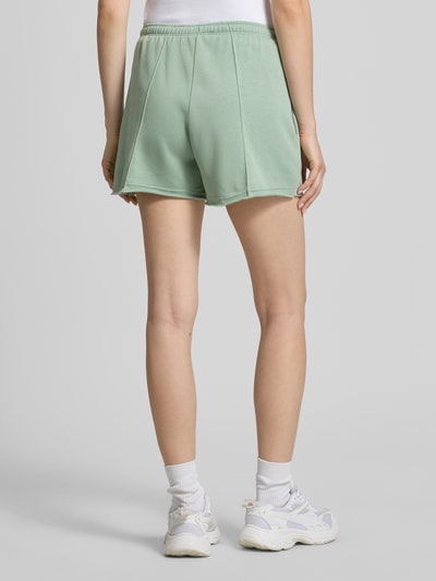 Frauenmodel trägt Regular Fit Shorts mit Tunnelzug von Nike aus Baumwoll-Mix in Mintgrün mit Logo-Stitching, abgerundete Passform, Ganzkörperansicht Rückansicht.