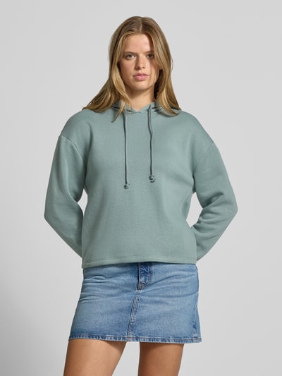Frauenmodel trägt Regular Fit Hoodie aus Baumwoll-Mix Modell 'CHILLI' von PIECES in Hellgrün, kombiniert mit Jeansrock, Ganzkörperansicht von vorne. Damen Hoodie von PIECES.
