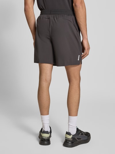 Männermodel trägt Shorts mit elastischem Bund und Logo von PUMA PERFORMANCE in Dunkelgrau, Material-Mix mit Stretch-Anteil, Ganzkörperansicht Rückansicht.