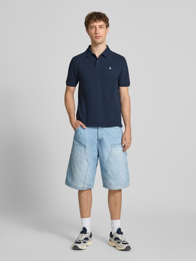 Männermodel trägt Modern Fit Poloshirt mit logo-stitching van REVIEW in donkerblauw katoenmix, polokraag, korte knoopsluiting, ruglengte bij maat M 65 cm, ganzlichaamsaanzicht van voren.