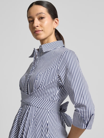 Modelka nosi Hemdblusenkleid mit Taillenband od Apricot, biało-granatowe paski, mieszanka bawełny i elastanu, krój slim fit, długość midi, kołnierzyk kent, rękaw 3/4, szerokość w rozmiarze S 40 cm, długość tyłu w rozmiarze S 110 cm, długość rękawa 50 cm, zbliżenie na górną część ciała z przodu.