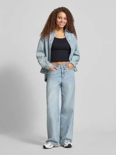 Frauenmodel trägt Slim Fit Top aus Baumwoll-Mix Modell 'ESSENTIAL RIBBED TANK' von Levi's® in Schwarz, kombiniert mit hellblauer Jeans und Overshirt; unifarbene Optik, U-Ausschnitt, Label Patch, Feinripp-Struktur; Ganzkörperansicht von vorne.