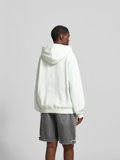 Männermodel trägt Oversized Hoodie mit Logo-Stitching von Anine Bing aus reiner Baumwolle mit Kapuze und Känguru-Tasche, Oversized-Fit, Rückenlänge 64 cm, grau und weiß, Ganzkörperansicht Rückansicht.