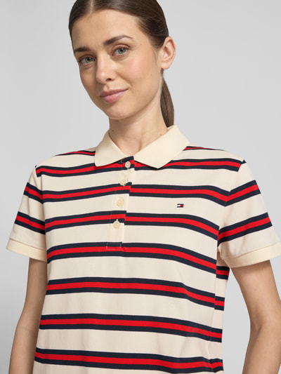 Frauenmodel trägt Regular Fit Poloshirt aus Baumwoll-Mix von Tommy Hilfiger, cremefarben mit roten und dunkelblauen Streifen, Logo-Detail, Polokragen, kurze Knopfleiste, Piqué-Textur, Nahaufnahme Oberkörper.