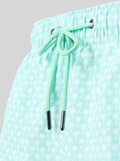 Männermodel trägt Badehose mit Gesäßleistentasche von MCNEAL, helles Türkis mit Palmenmuster, Elastischer Bund, Kordelzug, Nahaufnahme Oberschenkel.