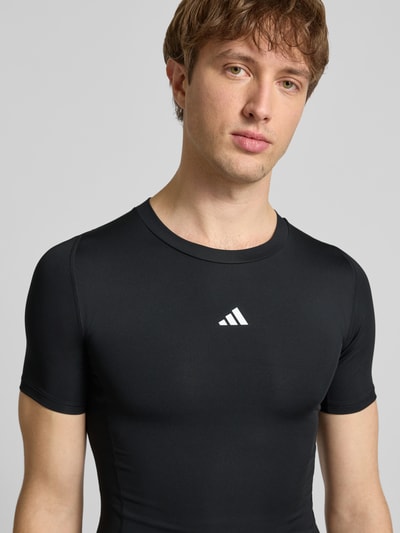 Männermodel trägt T-Shirt mit Label-Print von adidas Training, schwarz, Slim Fit, gerippter Rundhalsausschnitt, Nahaufnahme Oberkörper.