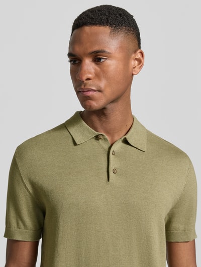 Mężczyznamodel nosi Regular Fit Poloshirt aus Bio-Baumwoll-Mix Modell 'BERG' od SELECTED HOMME, dzianinowy melanż, z polokołnierzykiem, krótki rękaw, krótka listwa guzikowa, końcówki rękawów i dół prążkowane, materiał z bawełny organicznej, kolor oliwkowy, zbliżenie na górną część ciała.