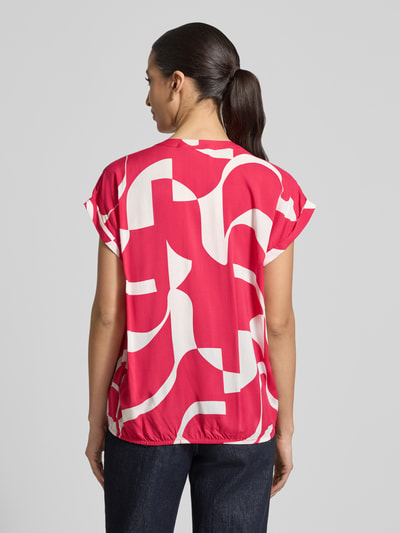 Frauenmodel trägt Regular Fit Bluse aus reiner Viskose Modell 'Miriama' von ZABAIONE, leuchtend rot mit weißen abstrakten Formen, Kurzärmelig, Tunika-Ausschnitt, elastischer Bund, Rückenlänge bei Größe S 62 cm, Ganzkörperansicht Rückansicht.