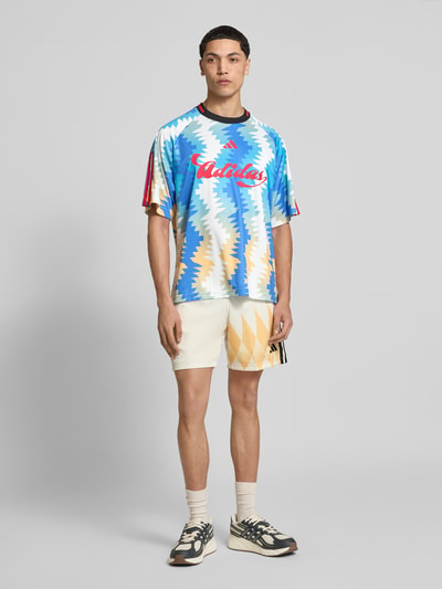 Männermodel trägt Regular Fit T-Shirt mit Allover-Muster von adidas Sportswear, Label-Print, Rundhals, Kurzarm, Ganzkörperansicht von vorne