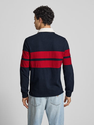 Männermodel trägt Regular Fit Rugby Shirt mit Logo- und Motiv-Stitching von Superdry in Dunkelblau und Rot, reine Baumwolle, Ganzkörperansicht Rückansicht.