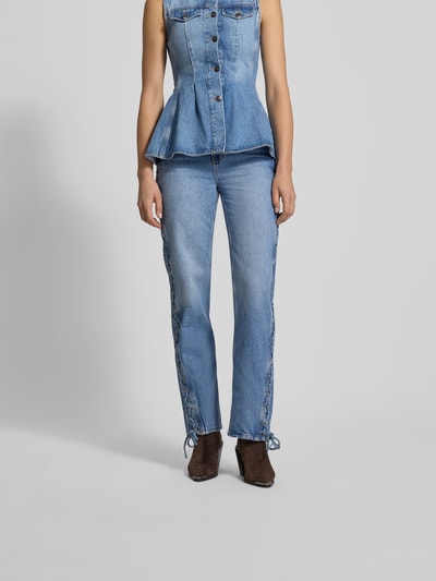 Frauenmodel trägt Straight Fit Jeans aus Baumwolle von ROTATE, Farbe Mittelblau, 5-Pocket-Design, seitliche Zier-Einsätze in Zopf-Optik, Ganzkörperansicht von vorne.