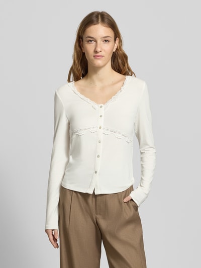 Frauenmodel trägt Slim Fit Langarmshirt aus Viskose-Mix Modell 'SINI' von Only in Unifarbe mit V-Ausschnitt, Knopfleiste und Spitzen-Details, Nahaufnahme Oberkörper.