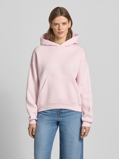 Vrouwenmodel draagt Regular Fit Hoodie met kangoeroezak model 'Iconic' van Gina Tricot in lichtroze, katoenmix, regular fit, elastische boorden, dames, voorkant, volledige lichaamsweergave.