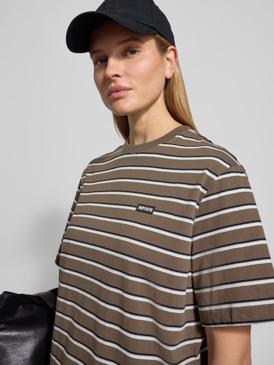 Frauenmodel trägt Oversized T-Shirt mit Logo-Patch von ROTATE aus reine Baumwolle, braun mit weißen Streifen, Rundhalsausschnitt, Kurzärmeliges Design, Oversized-Fit, Rückenlänge bei Größe S: 70 cm, Nahaufnahme Oberkörper.
