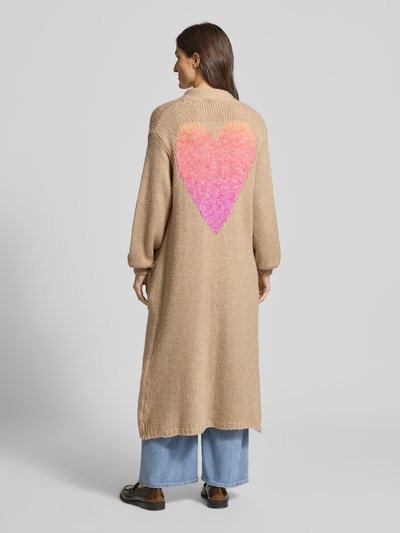 Frauenmodel trägt Longcardigan mit Eingrifftaschen von miss goodlife aus Baumwoll-Alpaka-Mix, beige mit pink-orangefarbenem Herz, lockerer Schnitt, gerippte Abschlüsse, Ganzkörperansicht Rückansicht.