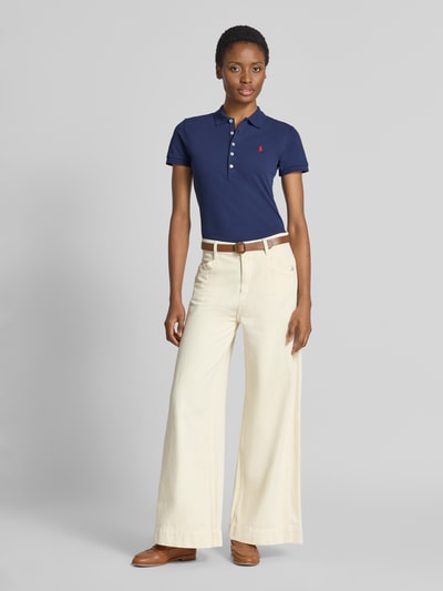 Frauenmodel trägt Slim Fit Poloshirt aus Baumwoll-Mix von Polo Ralph Lauren in Dunkelblau, kombiniert mit heller weiter Hose, Ganzkörperansicht von vorne.