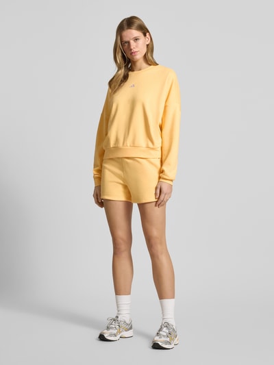 Frauenmodel trägt Sweatshirt mit Logo und Rundhalsausschnitt von adidas Sportswear im Relaxed Fit, Baumwoll-Mix, softes Gelb, Ganzkörperansicht von vorne.