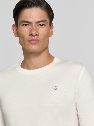 Männermodel trägt Shaped Fit Langarmshirt aus reiner Baumwolle von Marc O'Polo in Creme mit kleinem Logo, Nahaufnahme Oberkörper.