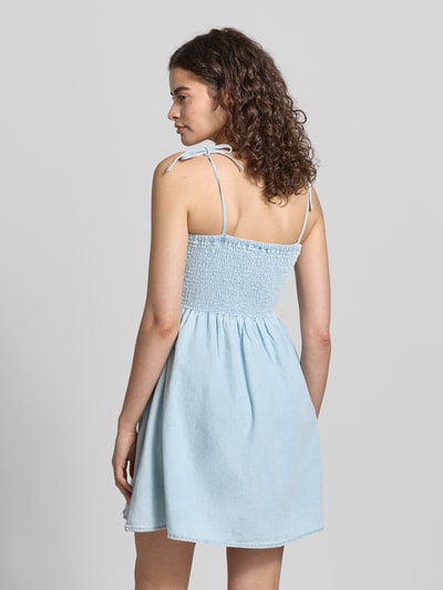Frauenmodel trägt Minikleid mit Smok-Detail Modell 'OREGON' von Noisy May, A-Linie, Denim-Optik, Reine Baumwolle, Rückenlänge 68 cm, Brustweite 35 cm, Träger mit Schnürung, Ganzkörperansicht Rückansicht.