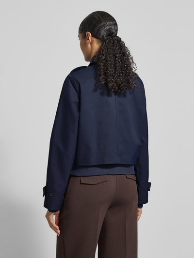 Vrouwenmodel draagt 'Trenchcoat mit Ärmelriegeln' van monari in donkerblauw, regular fit, dubbele knopenrij, mouwen met strook, rechte rug, bruine broek, recht en glad oppervlak, detailinformatie conform maat 36; volledig beeld van achteren.