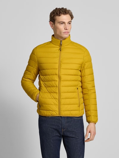 Męski model nosi Steppjacke mit Reißverschluss od MCNEAL w regularnym kroju, kolor musztardowy, stebnowana faktura, widok z przodu, zdjęcie całej sylwetki.