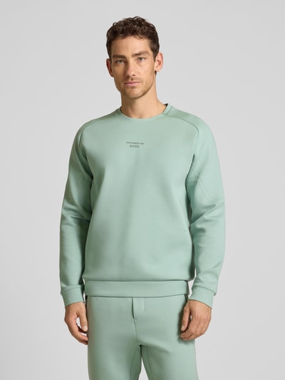 Männermodel trägt Regular Fit Sweatshirt aus Baumwoll-Mix Modell 'SW_PS SPIRIT70 CN' von BOSS Green X Porsche, Unifarbe mint, 3D-Label Print, Rundhalsausschnitt, langarm, gerippte Abschlüsse, Sweat-Material, Ganzkörperansicht von vorne.