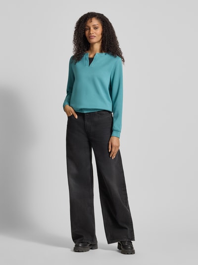Frauenmodel trägt Regular Fit Sweatshirt mit Viskose-Anteil von Tom Tailor in Optik: Unifarben, Label-Stitching-Applikation, Strasssteine, V-Ausschnitt, Langarm, elastischer Ärmelabschluss, elastischer Rumpfabschluss, Materialverarbeitung: Sweat, Ganzkörperansicht von vorne.